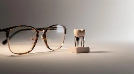 Gros plan symbolique sur une paire de lunettes et un modèle de couronne dentaire évoquant la question de la qualité du panier 100% Santé